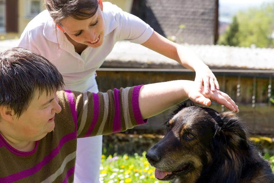 Two people pet a dog outside.