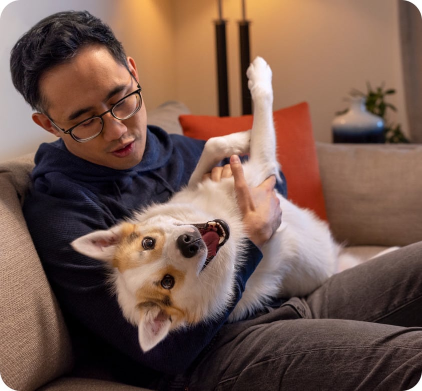 A man is sitting on a sofa with his pet dog in his arms.