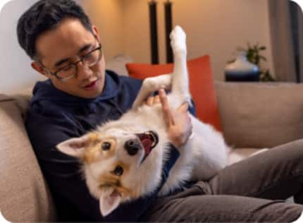 A man is sitting on a sofa with his pet dog in his arms.